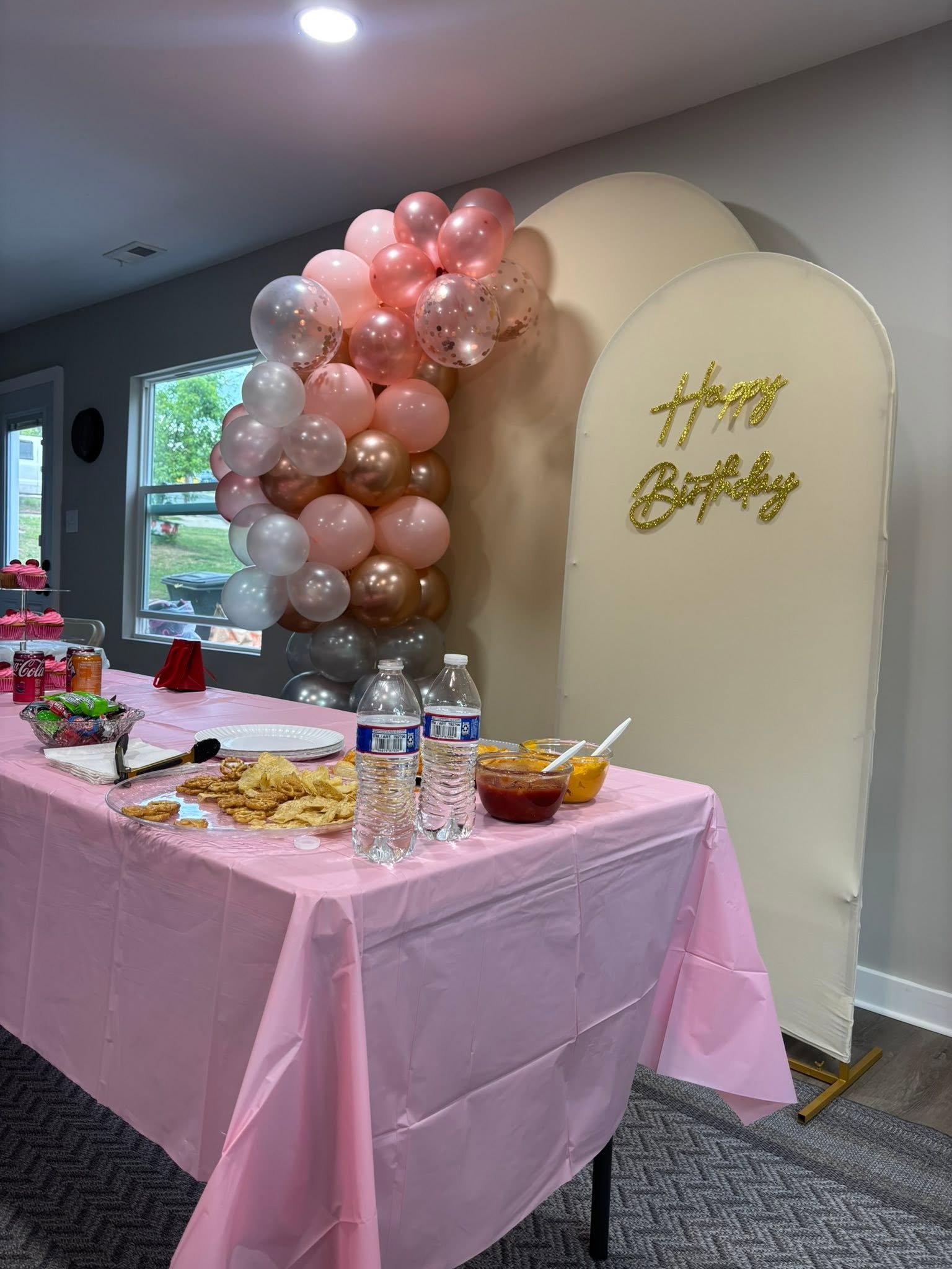 Decoración de cumpleaños con globos rosados, fondo con arcos y mesa de dulces